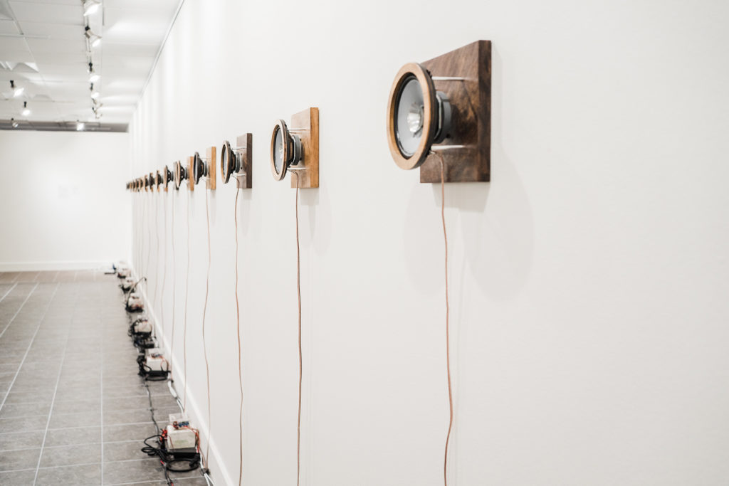 Wildfire sound art installation. 16 speakers along a white wall, playing back sounds of fire at speeds of wildfires