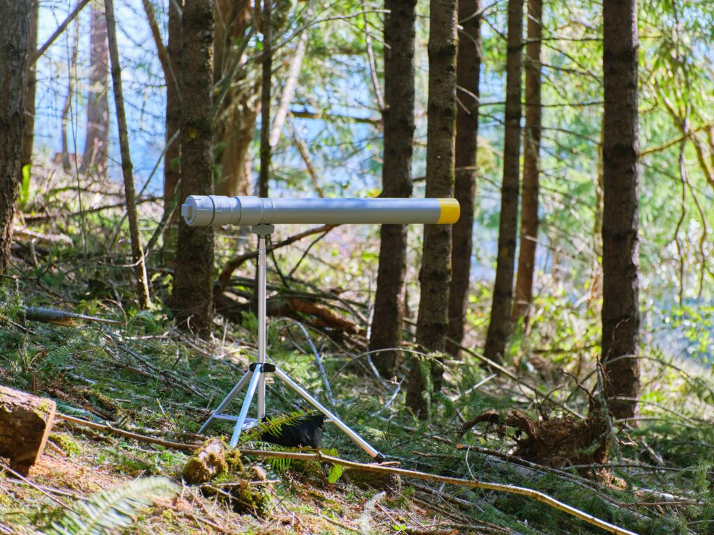 PVC sound cannon on tripod painted gray with a yellow tip of barrel. Situated in the woods