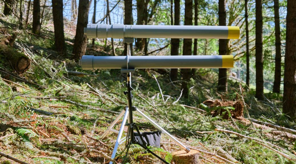 Two PVC sound cannons on tripods painted gray with a yellow tip of barrel. Situated in the woods