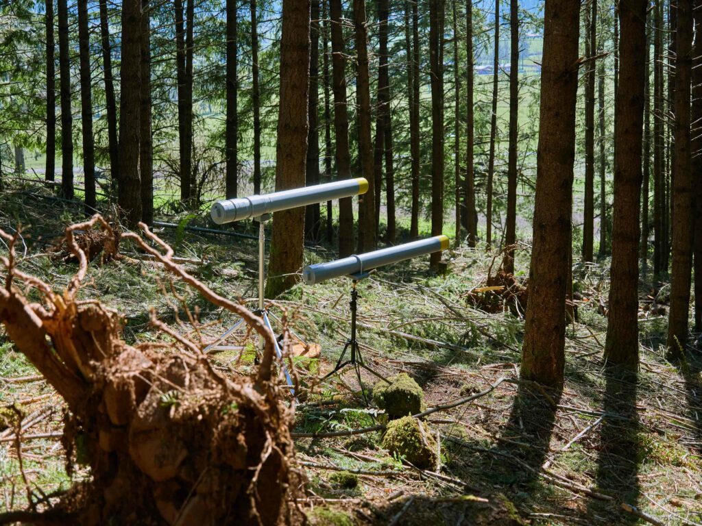Two PVC sound cannons on tripods painted gray with a yellow tip of barrel. Situated in the woods
